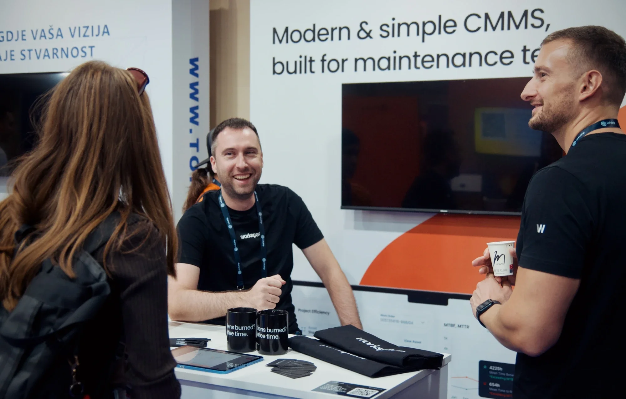 Workspace merch at Infobip Shift 2026: mugs with the line "Tokens burned? Coffee time.", canvas tote bags and T-shirts on the booth counter